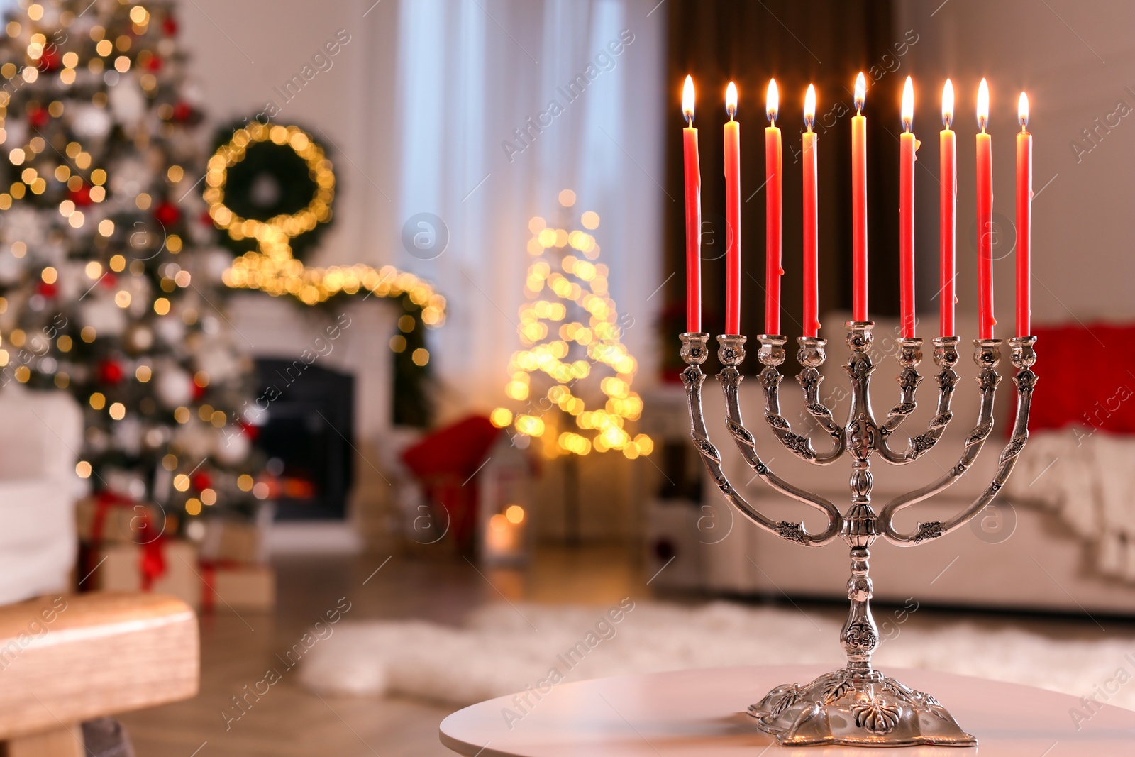 Photo of Silver menorah on white table in room with fireplace and Christmas decorations. Hanukkah symbol