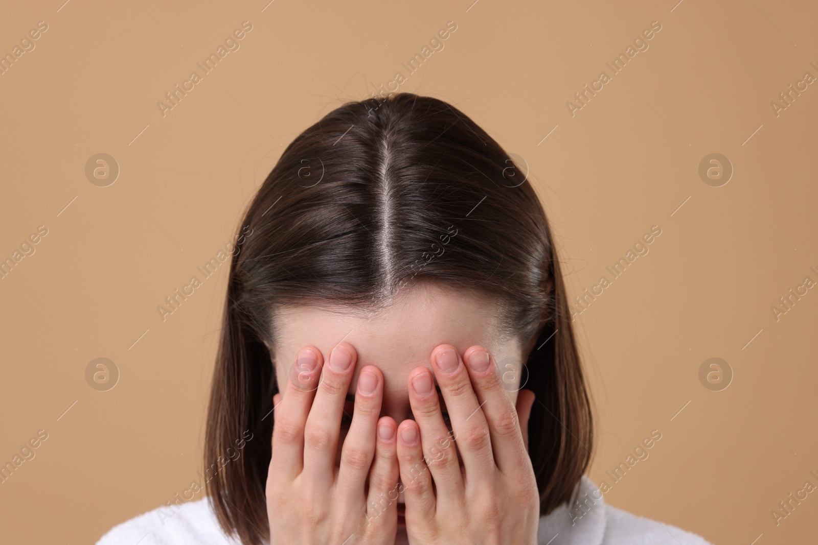 Photo of Woman suffering from hair loss problem on light brown background