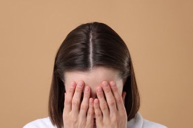 Woman suffering from hair loss problem on light brown background