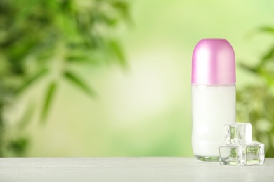 Photo of Deodorant container and ice cubes on white wooden table against blurred background. Space for text