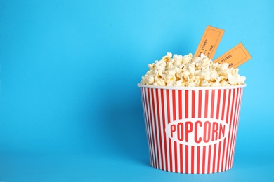 Photo of Bucket of fresh tasty popcorn and tickets on color background, space for text. Cinema snack