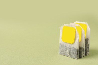 Photo of Paper tea bags with tags on light green background, space for text