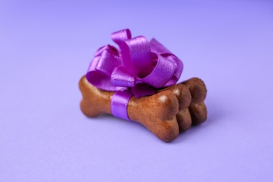 Photo of Bone shaped dog cookies with beautiful bow on purple background, closeup