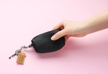 Photo of Woman holding leather case with key on pink background, top view