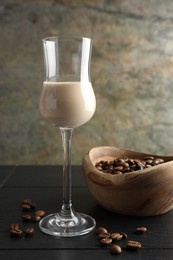 Photo of Coffee cream liqueur in glass and beans on black wooden table