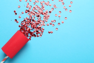 Photo of Red confetti and party cracker on light blue background, above view. Space for text