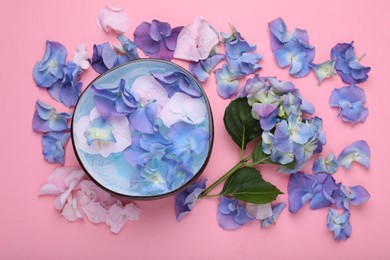 Spa composition. Aromatic water in bowl and flowers on pink background, flat lay