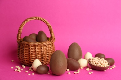 Sweet chocolate eggs and wicker basket on pink background