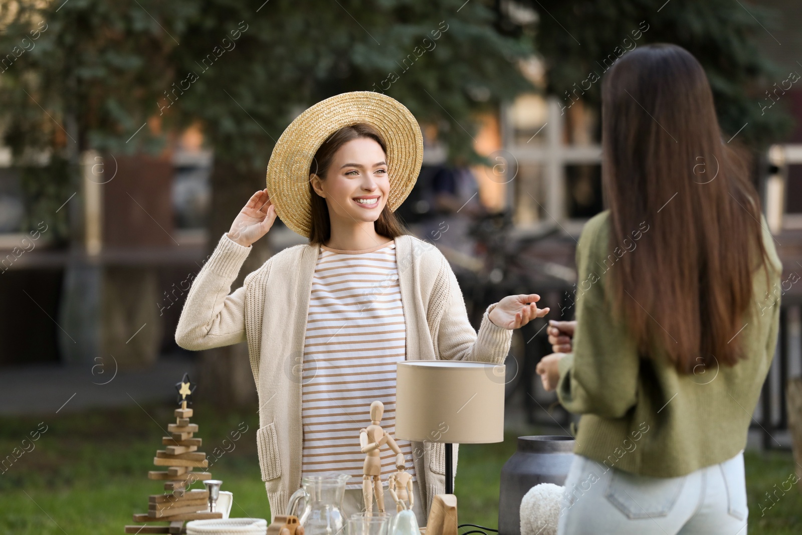 Photo of Women shopping on garage sale near table with different items in yard