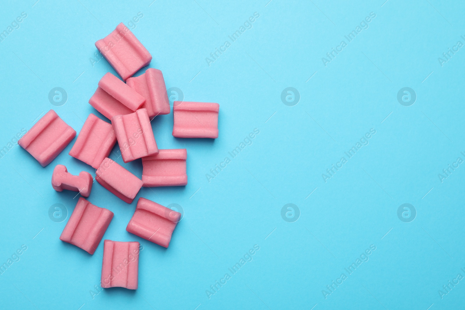 Photo of Tasty pink chewing gums on light blue background, flat lay. Space for text