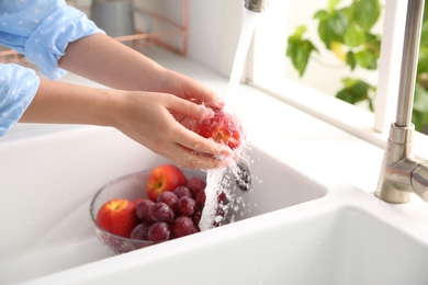 Photo of Woman washing fresh nectarine in kitchen sink, closeup