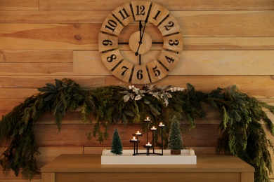 Photo of Christmas decor on console table near wooden wall with clock and garland. Interior design