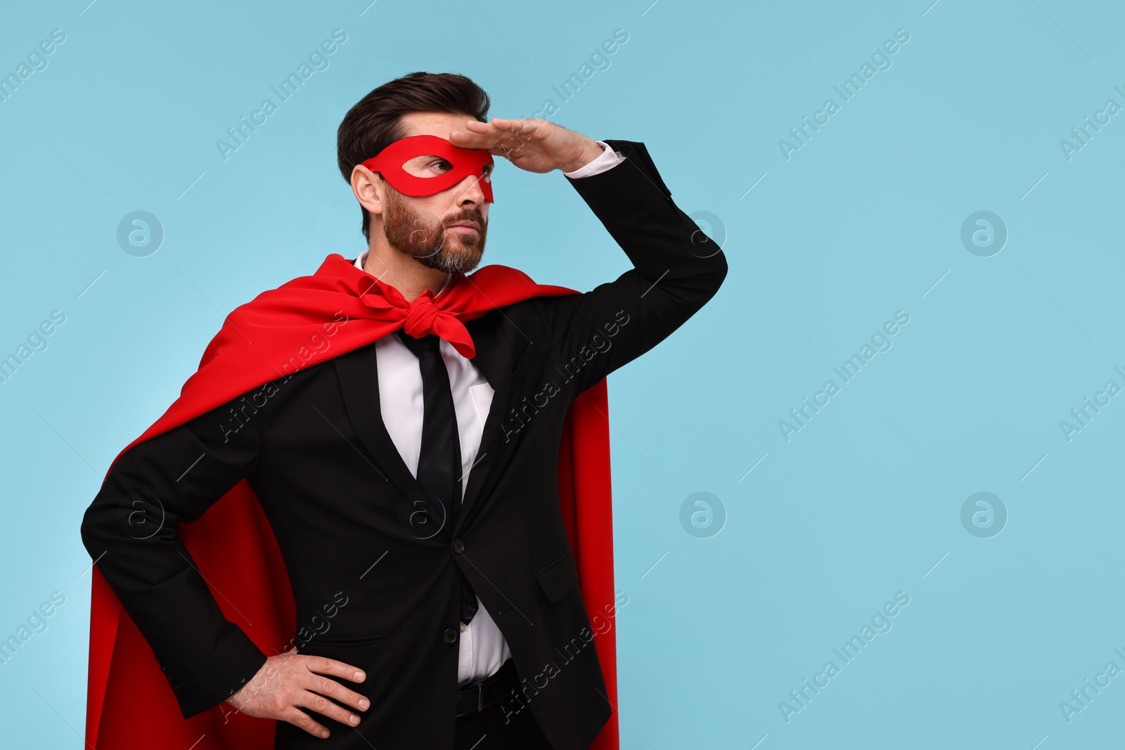 Photo of Businessman wearing red superhero cape and mask on light blue background. Space for text