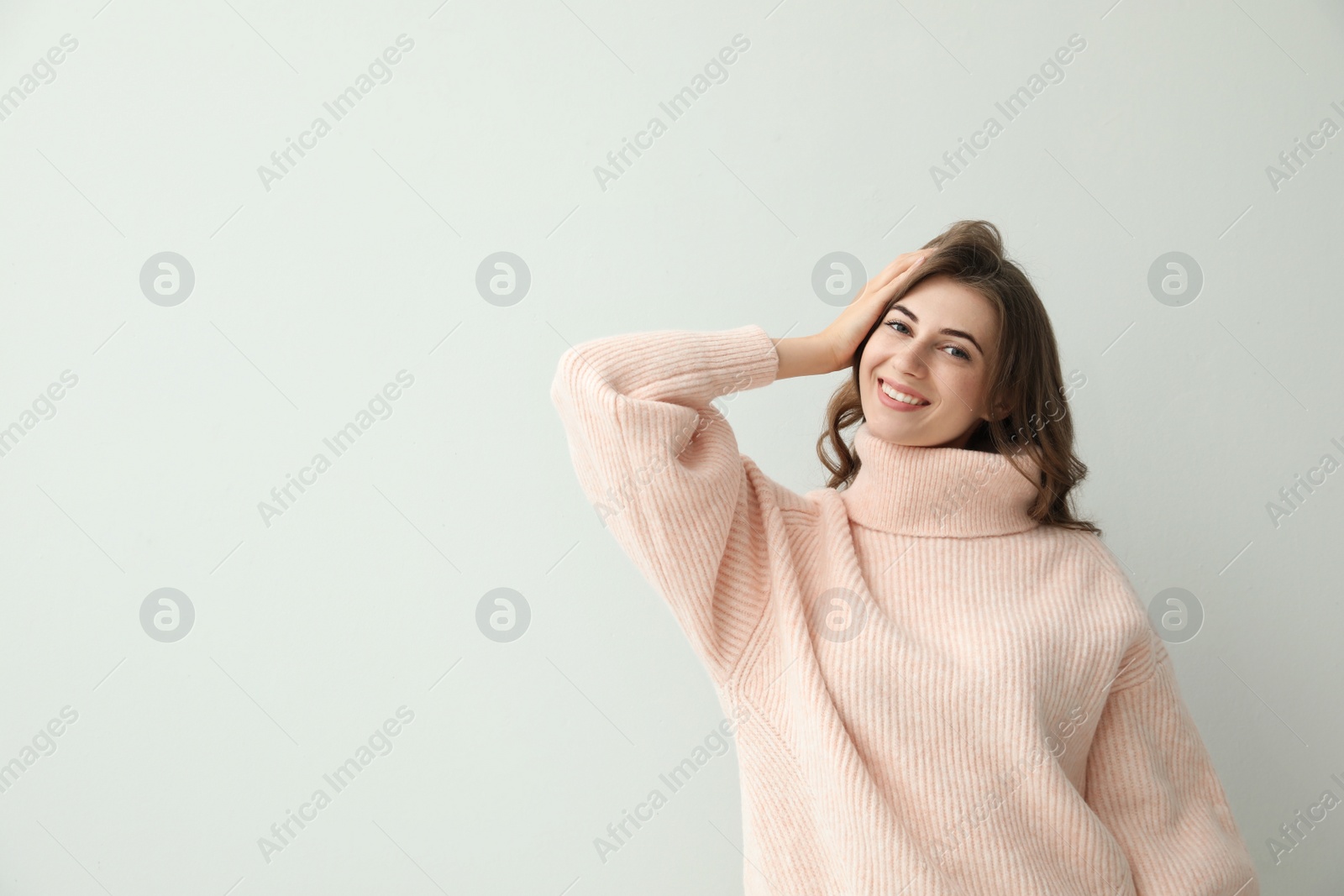 Photo of Beautiful young woman wearing warm pink sweater on light background. Space for text