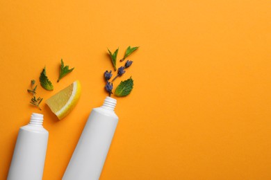 Photo of Blank tubes of toothpaste with herbs, lemon and lavender flowers on orange background, flat lay. Space for text