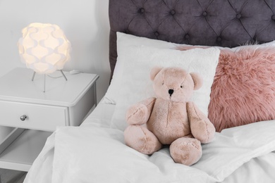 Photo of Cute teddy bear sitting on bed indoors. Space for text