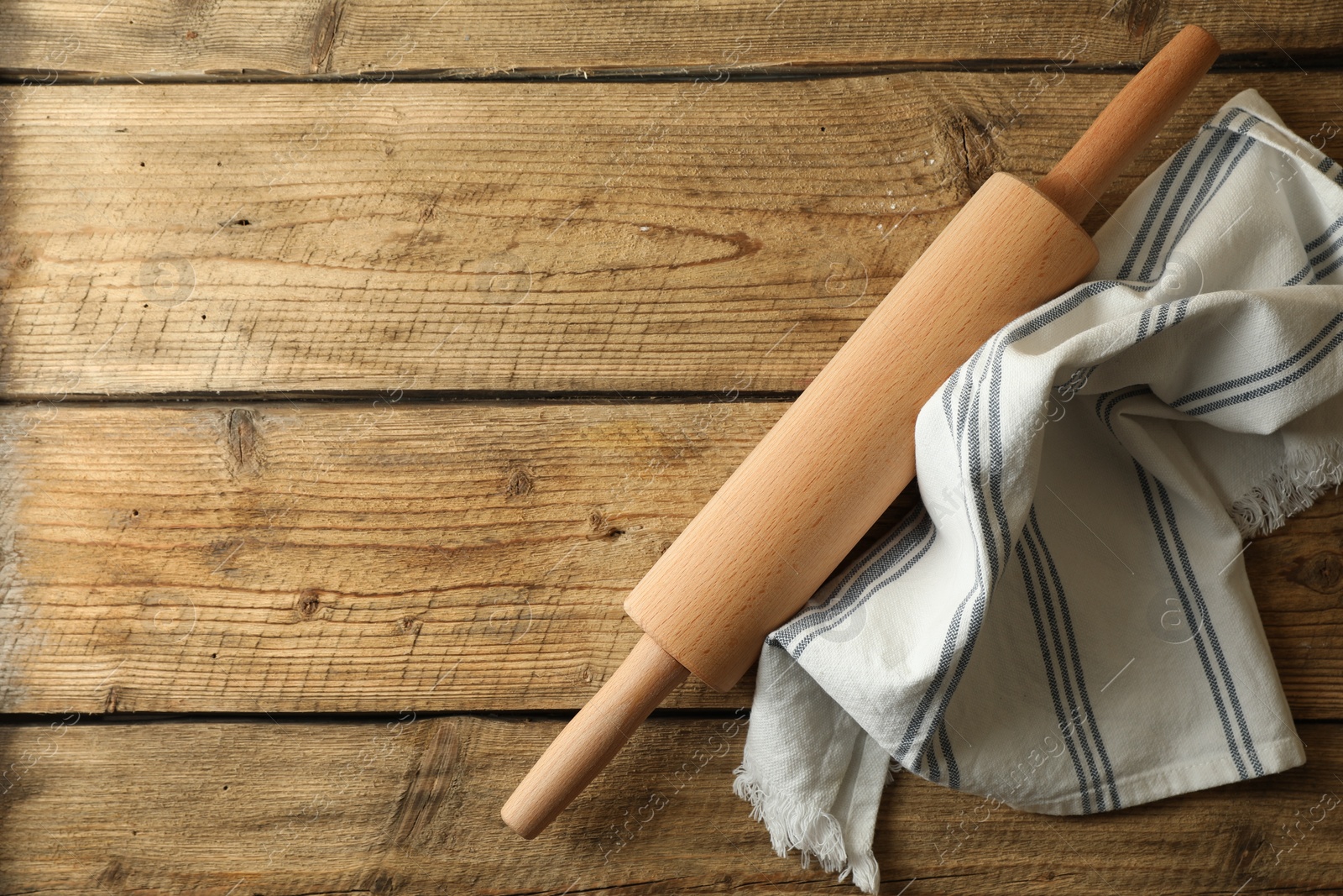 Photo of Rolling pin and kitchen towel on wooden table, top view. Space for text