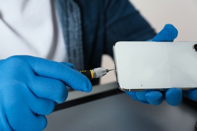 Technician repairing broken smartphone at table, closeup