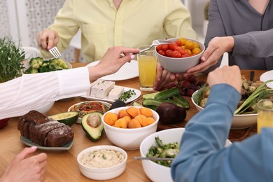 Photo of Friends eating vegetarian food at wooden table indoors, closeup