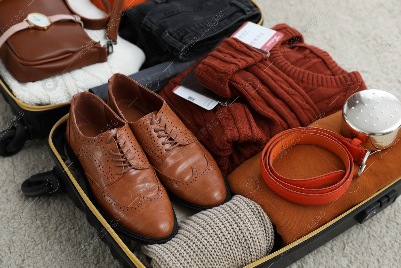 Photo of Open suitcase with folded clothes, accessories and shoes on floor, closeup