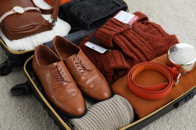 Photo of Open suitcase with folded clothes, accessories and shoes on floor, closeup