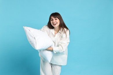 Happy woman in pyjama holding pillow on light blue background