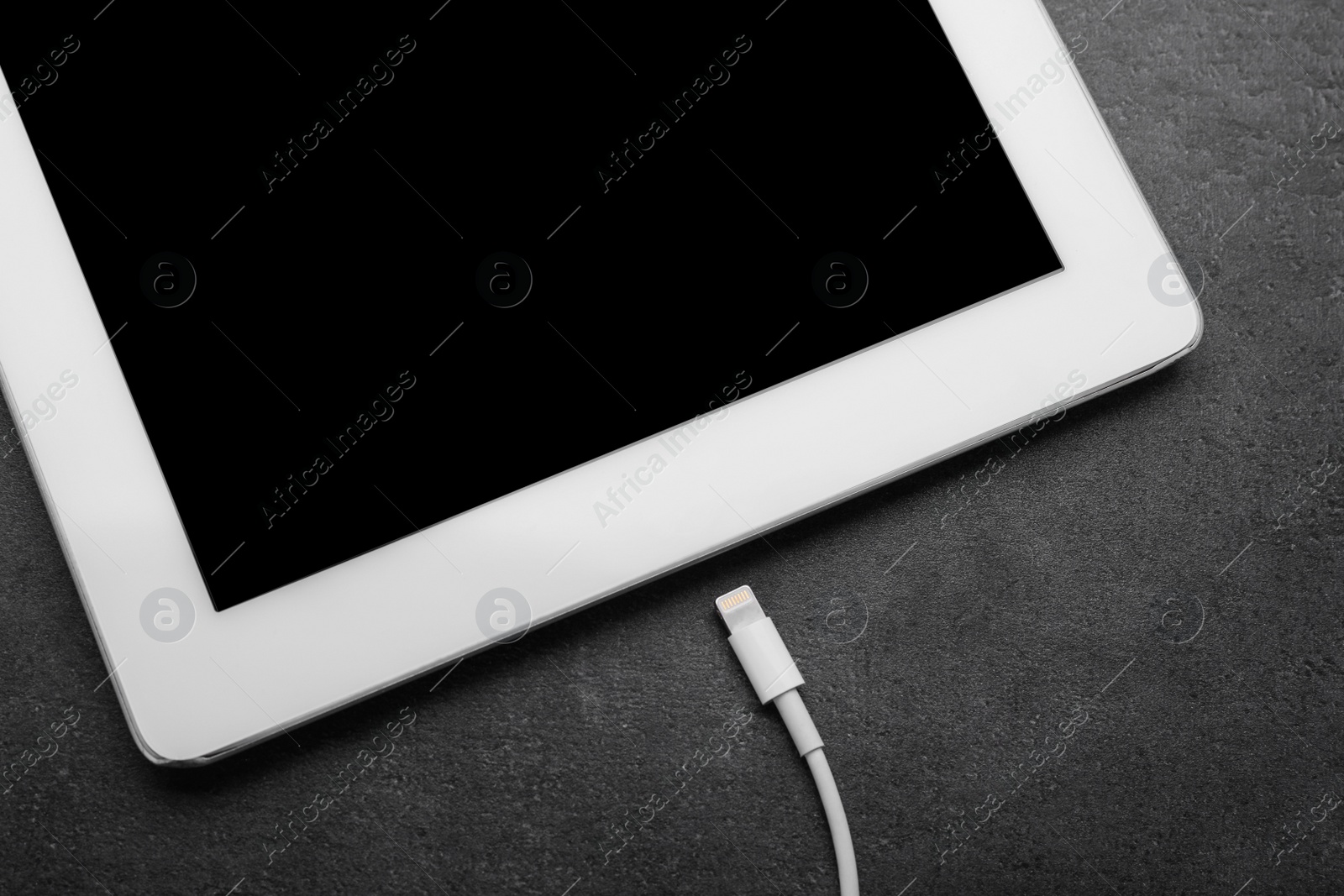 Photo of USB cable with lightning connector and tablet on dark table, closeup