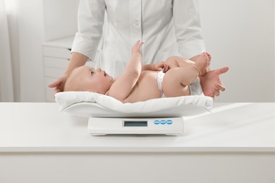 Pediatrician weighting cute little baby in clinic, closeup