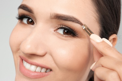 Photo of Young woman plucking eyebrow with tweezers, closeup