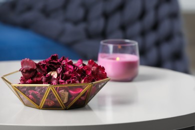 Aromatic potpourri of dried flowers in bowl and burning candle on table indoors, space for text