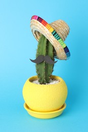 Photo of Cactus with Mexican sombrero hat and fake mustache on light blue background