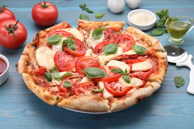 Photo of Delicious Caprese pizza and ingredients on blue wooden table, closeup
