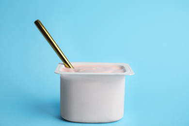 Photo of Tasty organic yogurt with spoon on light blue background