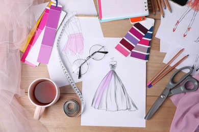 Sketches of clothes and different stuff on wooden table, flat lay. Fashion designer's workplace