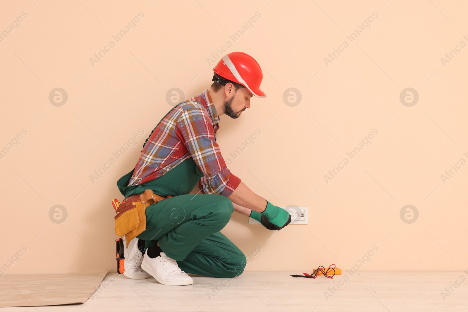 Photo of Electrician in uniform with screwdriver repairing power socket indoors