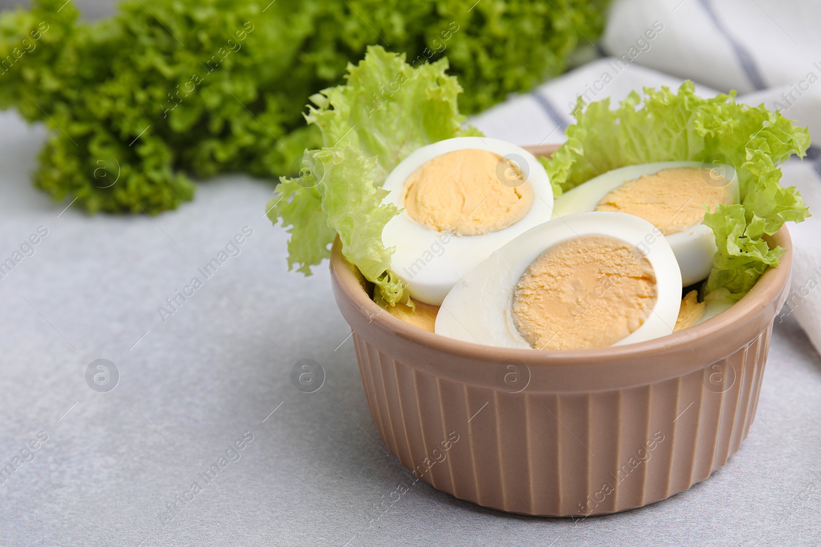 Photo of Fresh hard boiled eggs and lettuce on light grey table, closeup. Space for text