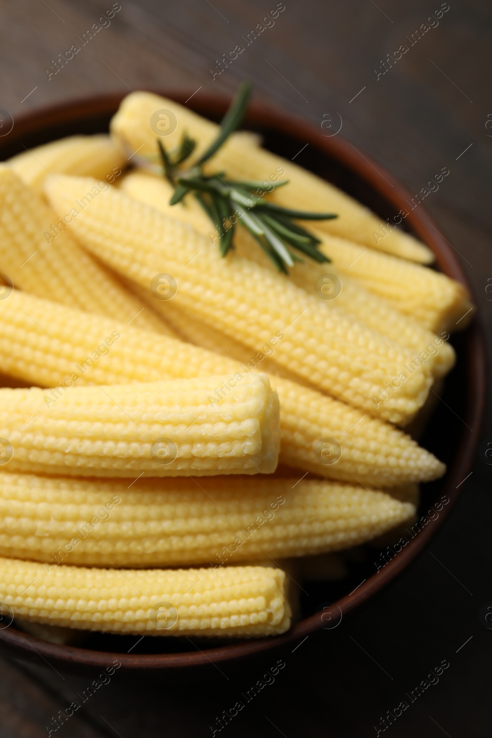 Photo of Tasty fresh yellow baby corns in bowl on wooden table, closeup