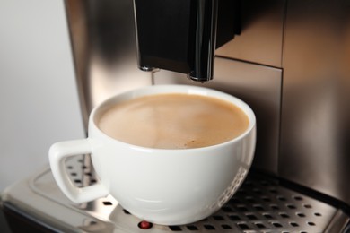 Espresso machine with cup of fresh coffee on drip tray against light background, closeup