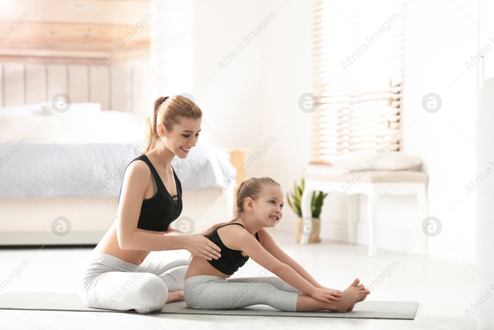 Photo of Mother and daughter in matching sportswear doing yoga together near bed at home