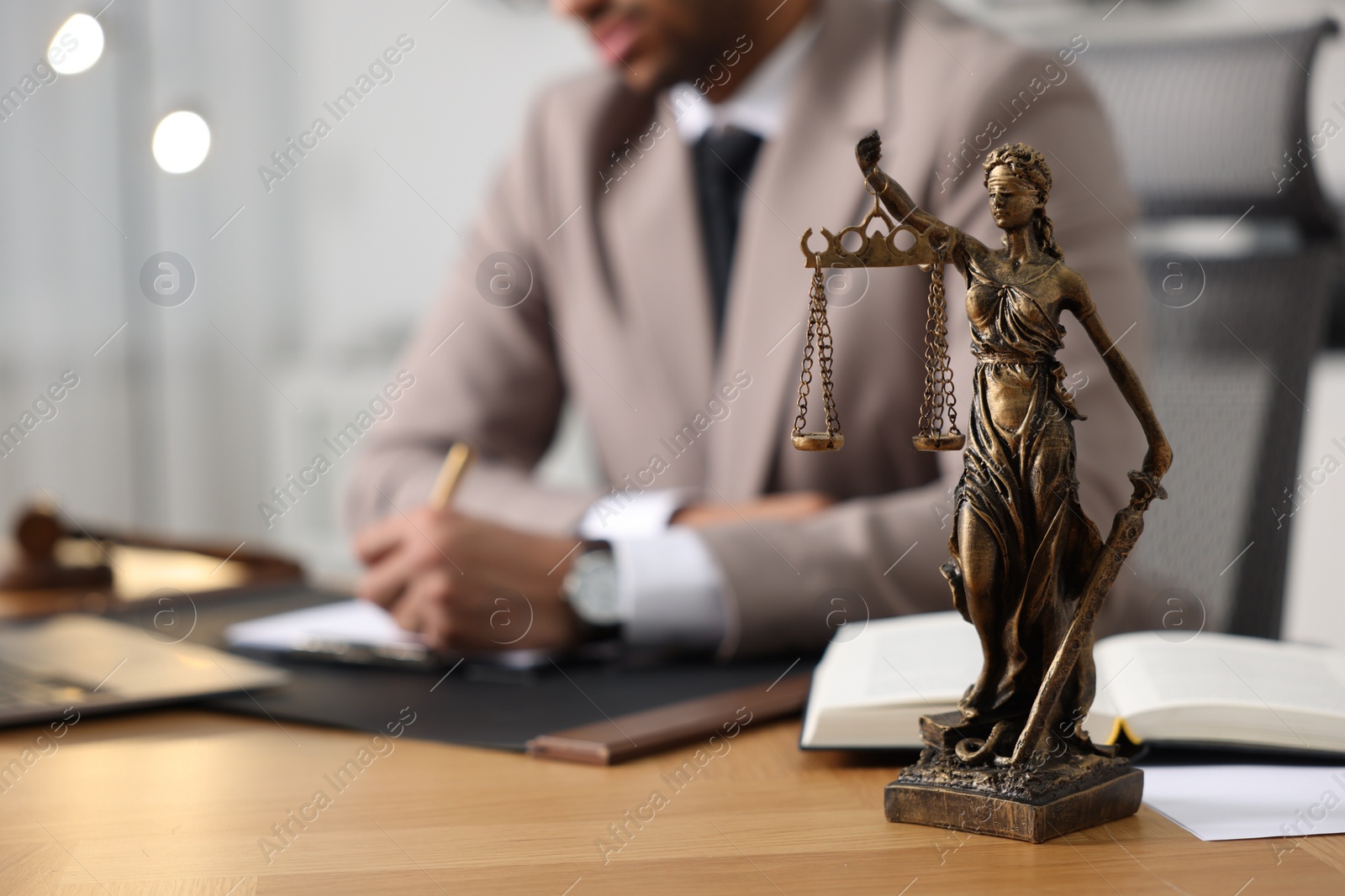 Photo of Lawyer working at table in office, focus on statue of Lady Justice