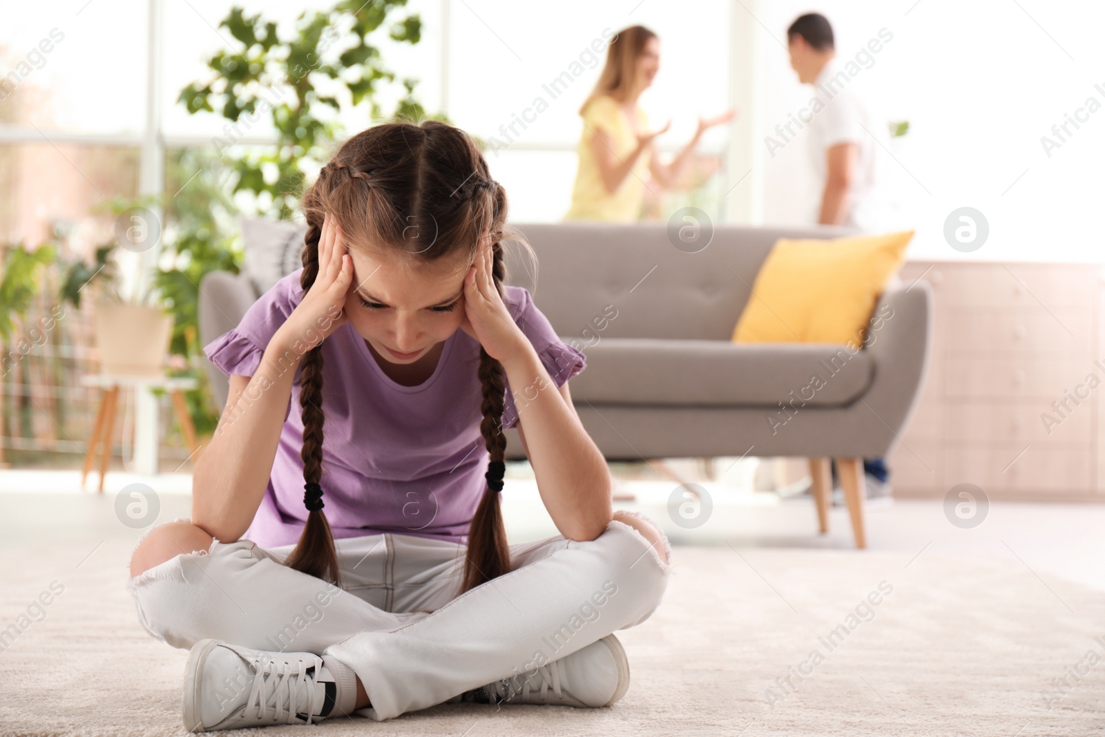 Photo of Upset child sitting on floor while parents fighting on background. Family relationships