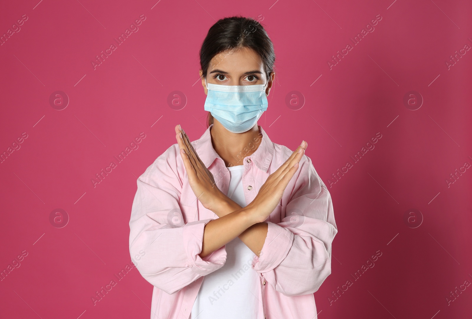 Photo of Woman in protective mask showing stop gesture on pink background. Prevent spreading of coronavirus