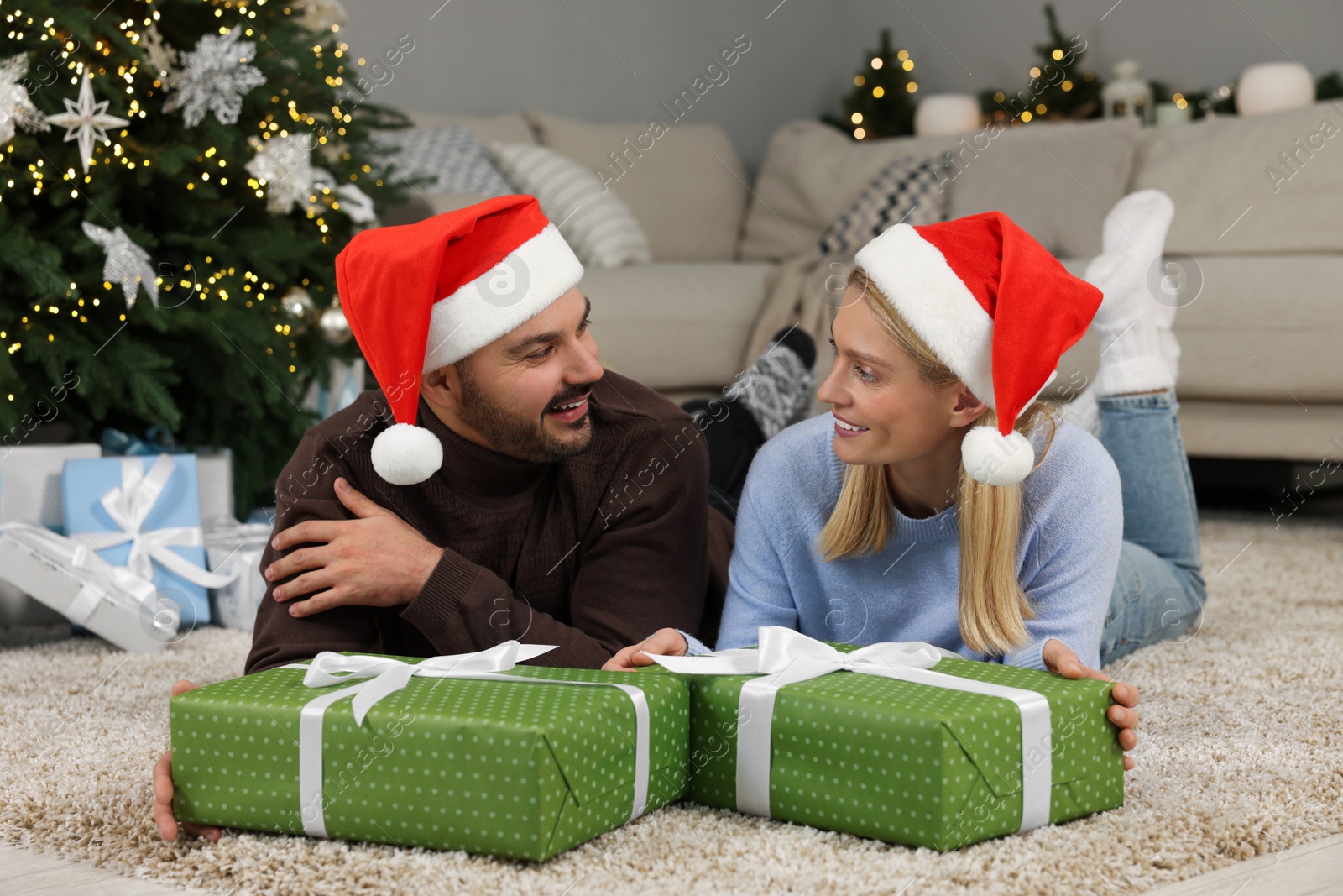 Photo of Happy couple in Santa hats with Christmas gifts at home