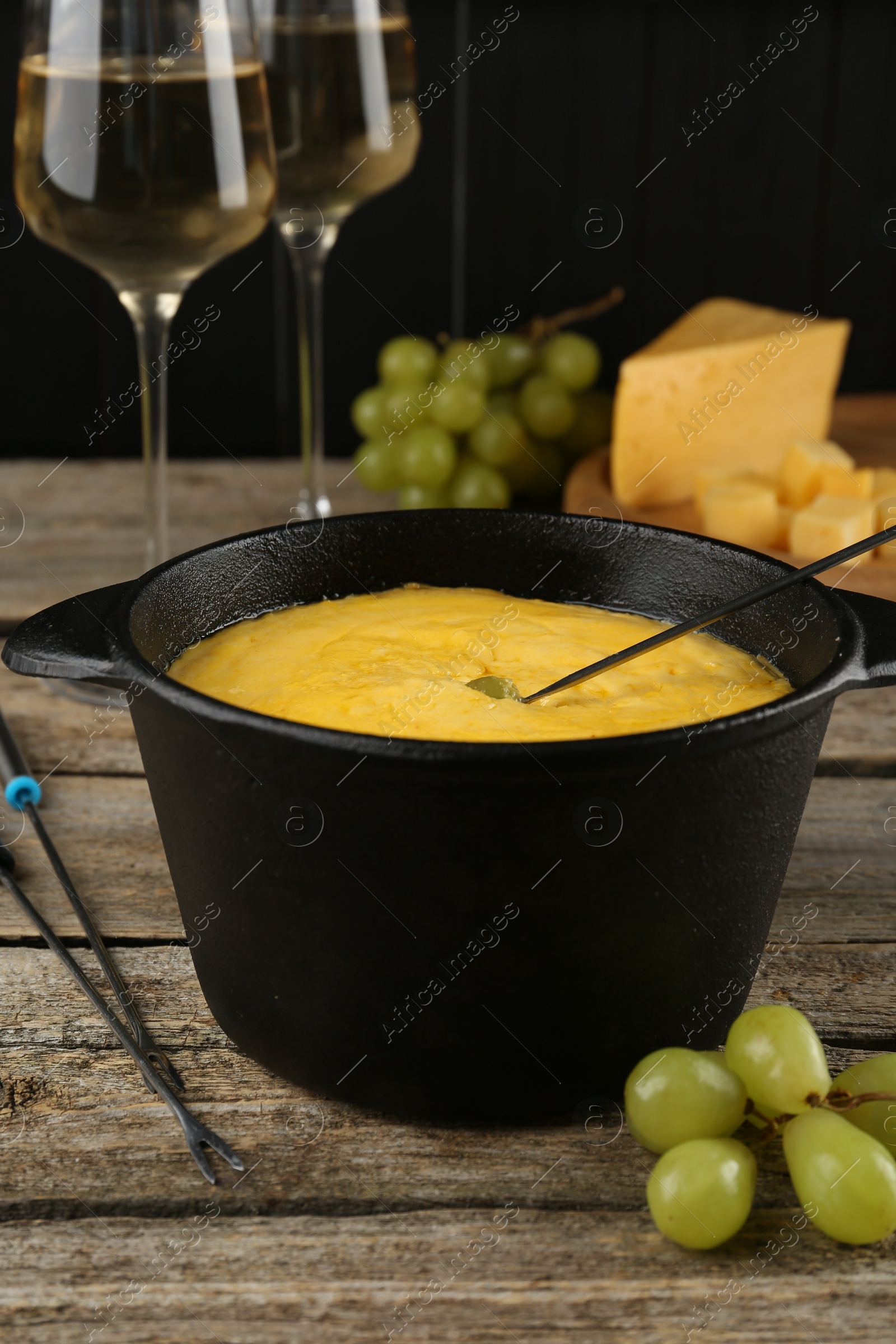 Photo of Fondue pot with melted cheese, glasses of wine and different products on wooden table