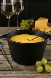 Photo of Fondue pot with melted cheese, glasses of wine and different products on wooden table
