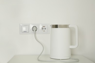 Photo of Electric kettle plugged into power socket on white wall