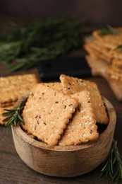 Photo of Cereal crackers with flax, sesame seeds and rosemary in bowl on wooden table, closeup
