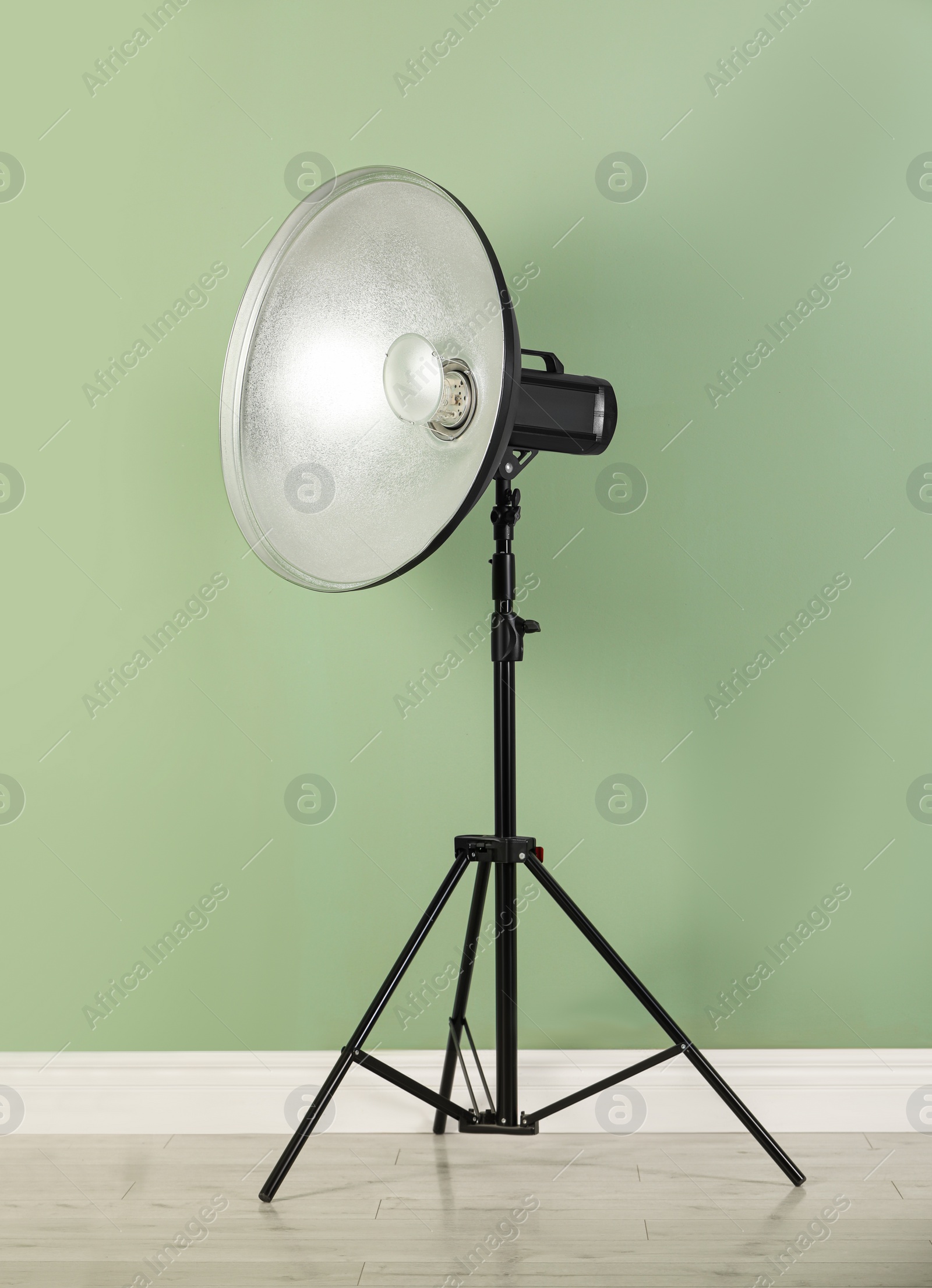 Photo of Professional beauty dish reflector on tripod near pale green wall in room. Photography equipment