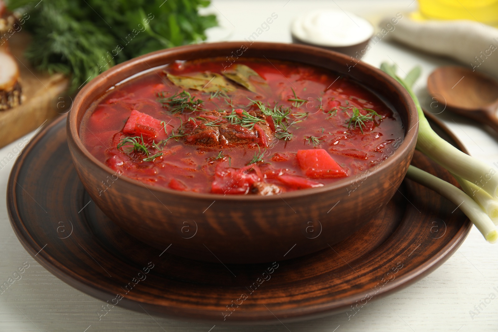 Photo of Stylish brown clay bowl with Ukrainian borsch served on white wooden table