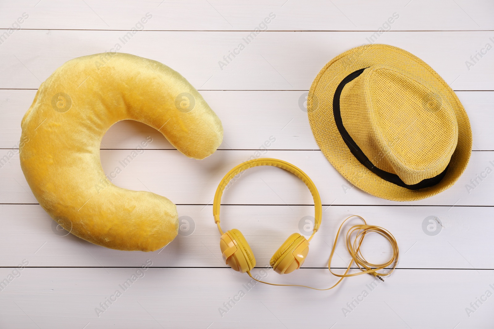 Photo of Yellow travel pillow, hat and headphones on white wooden background, flat lay